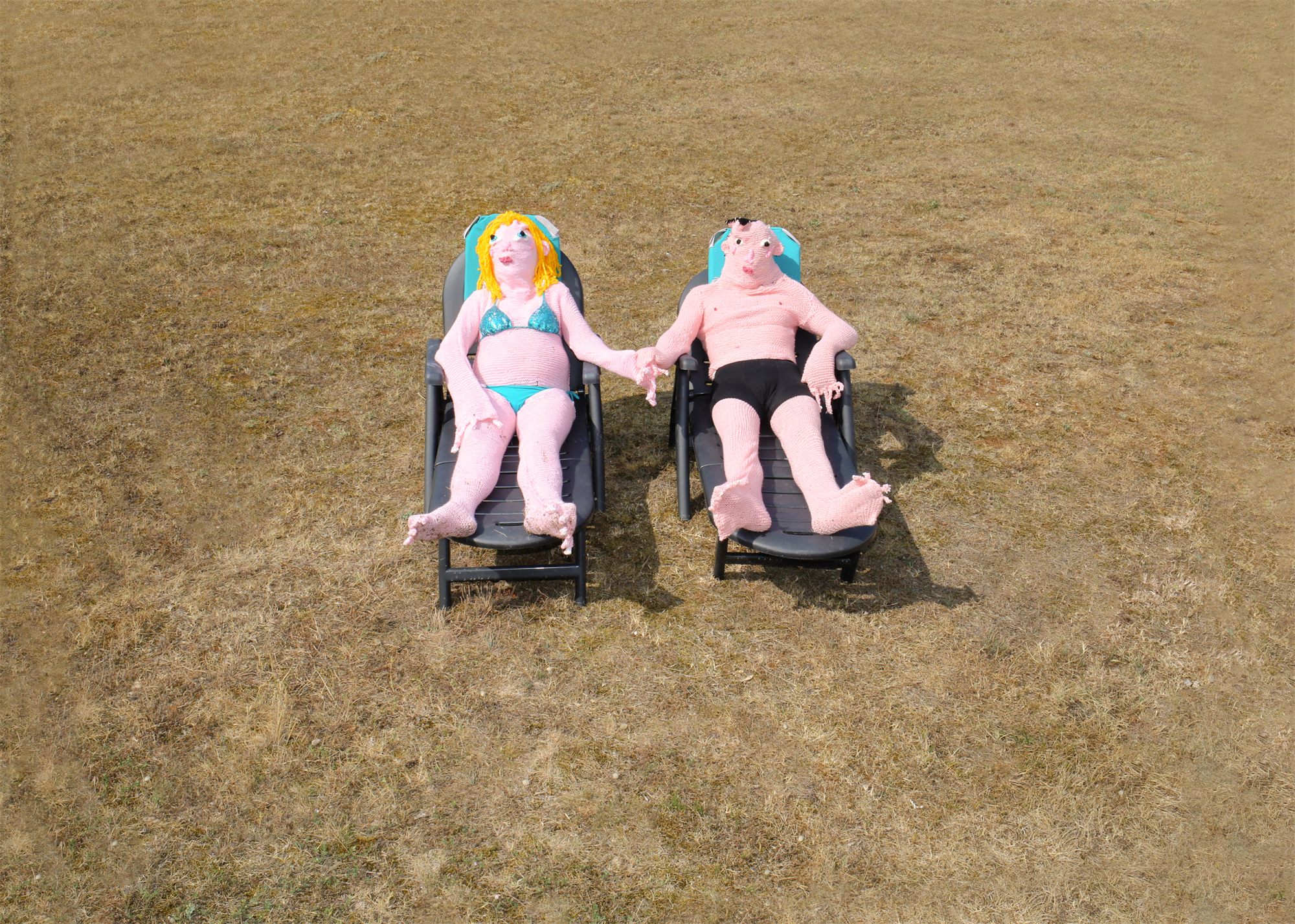 Éva Ostrowska, Hermits, pink knitted couple holding hands on sun loungers in a dry summer field, photographic performance