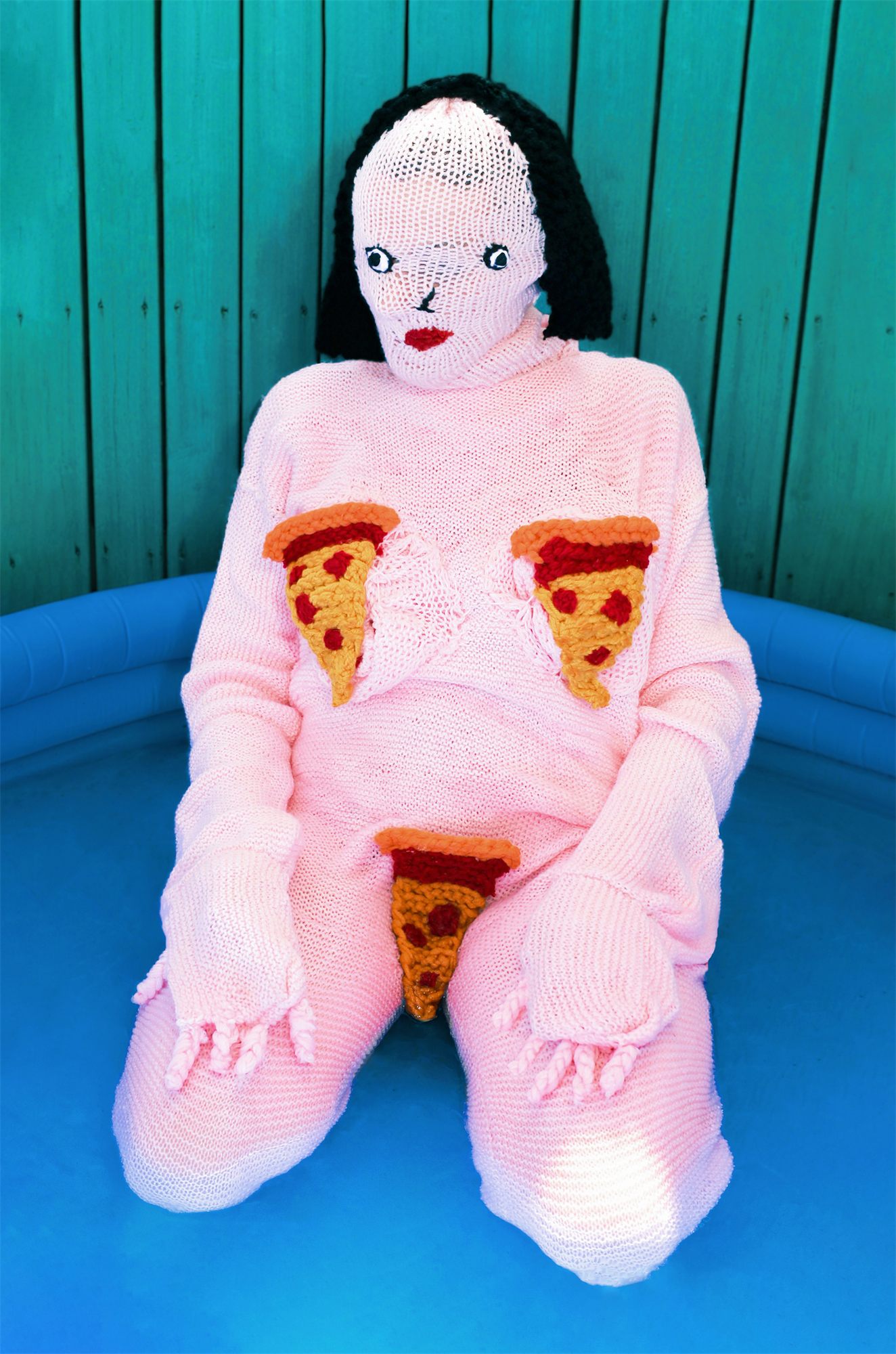 Éva Ostrowska, Pool Snacks, pink knitted figure with knitted pizza slices kneeling in a blue inflatable pool, photographic performance